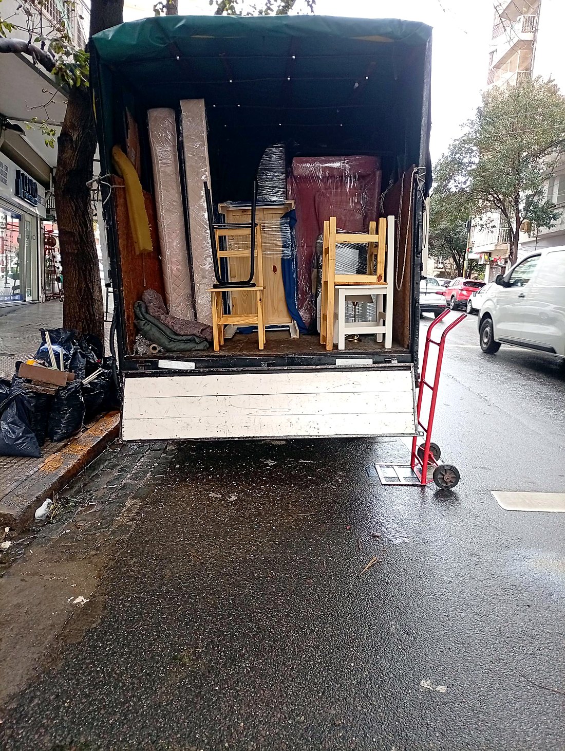 Camión de Fletes More con lona verde y tapa trasera cargado con colchones y muebles de pino