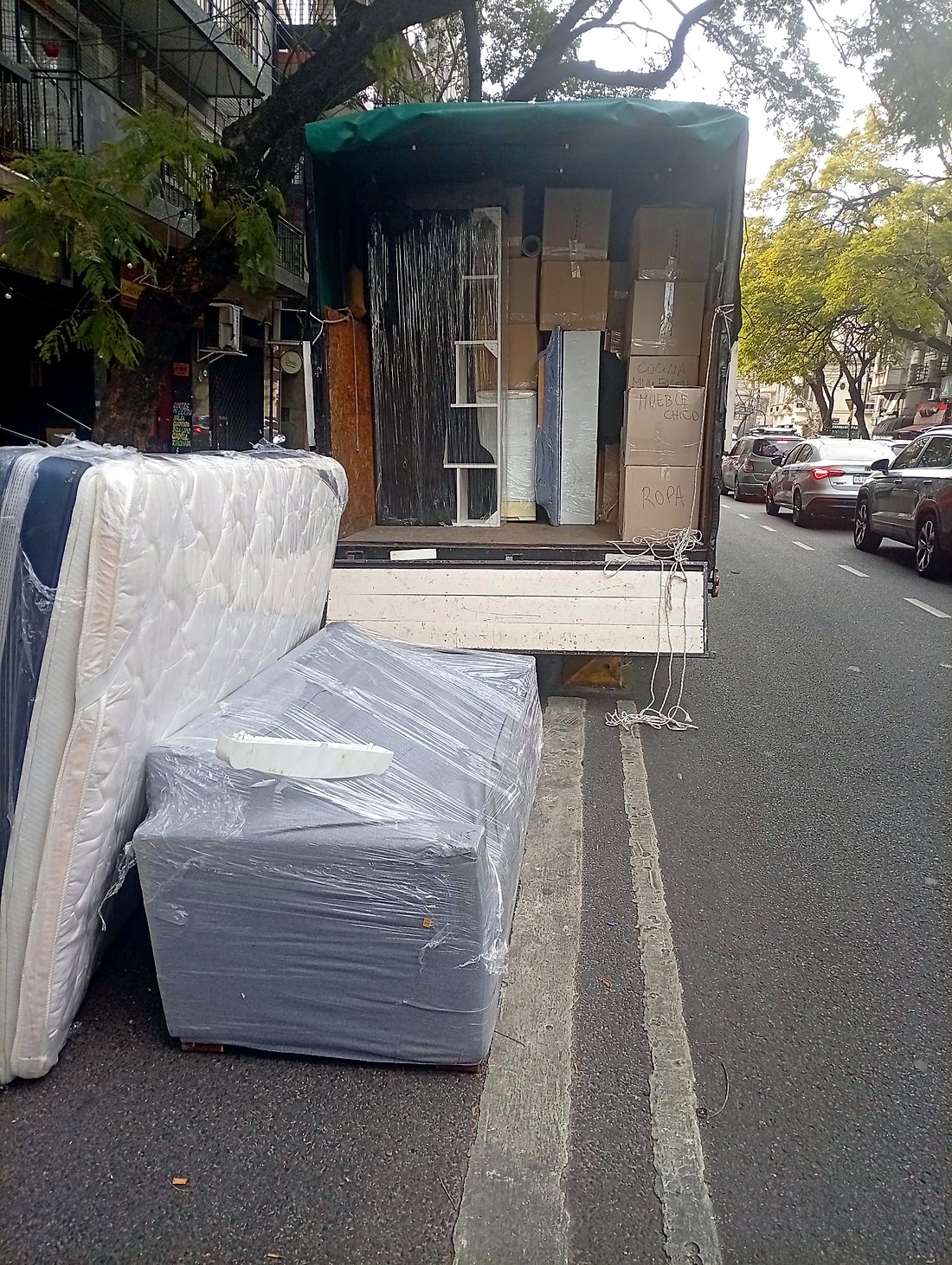 Mudanza de Fletes More en la calle: colchón y sillón embalados con film y camión con cajas rotuladas